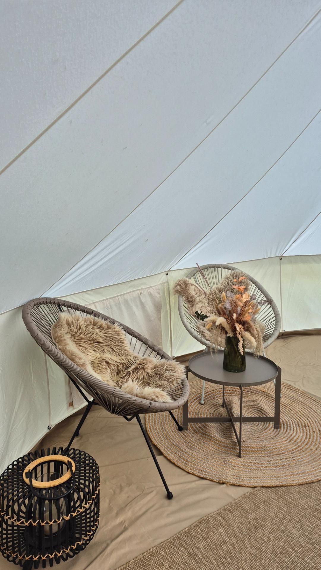 Gezellige zithoek met loungestoelen, schapenvachten en decoratie in een luxe glamping bell tent