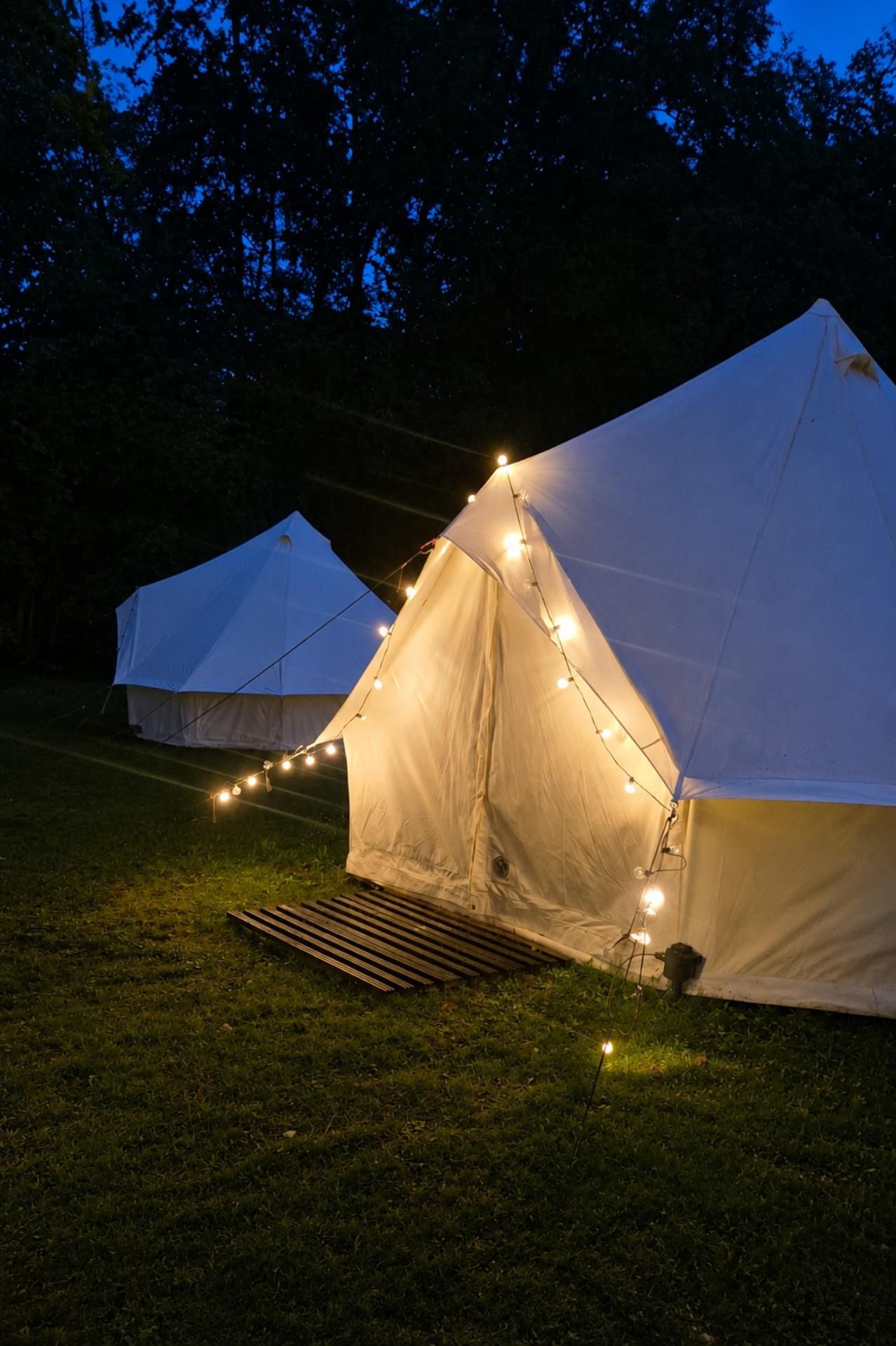 Verlichte glamping bell tent in de avond met warme sfeerverlichting op een groene camping