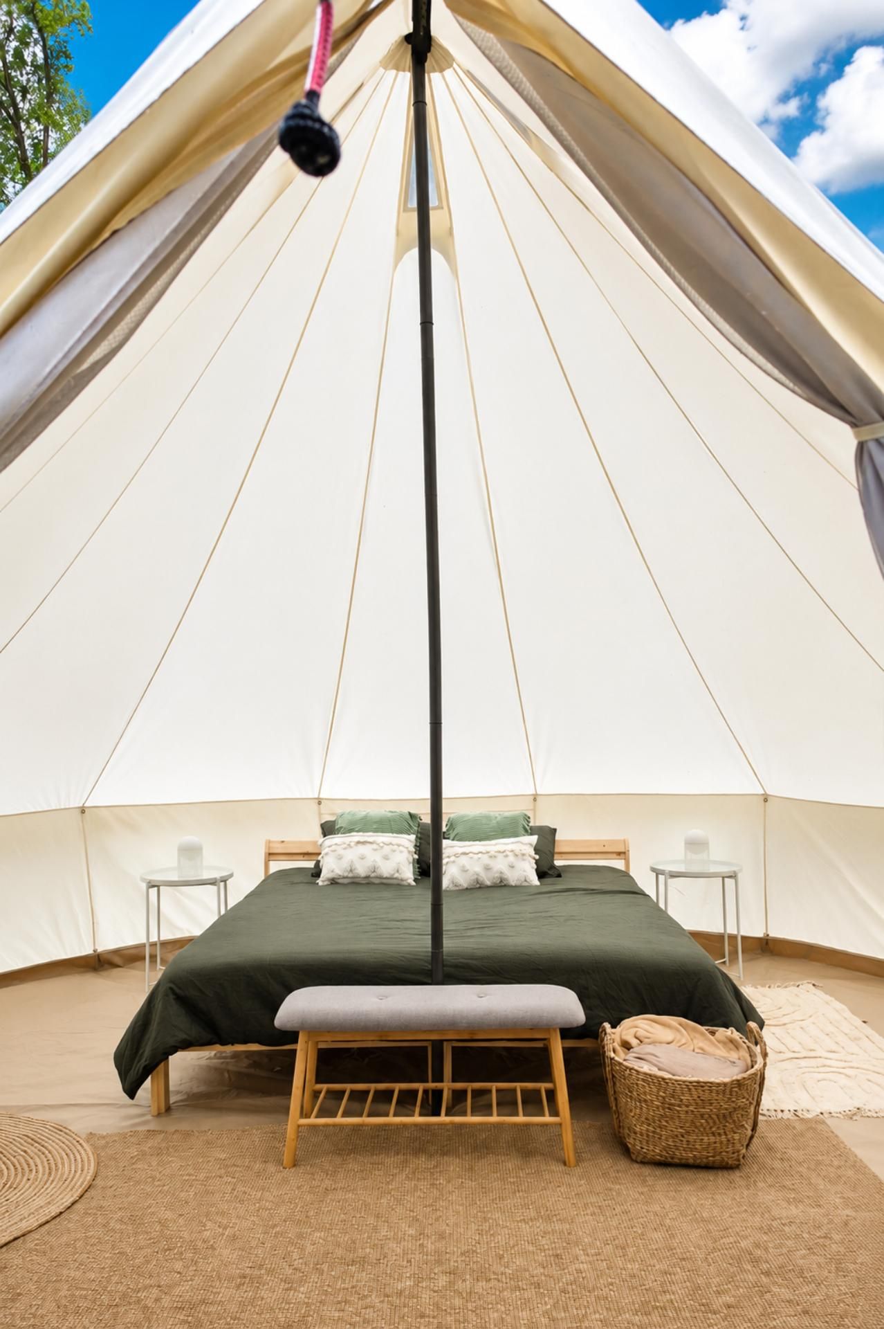 Stijlvol interieur van een glamping bell tent met tweepersoonsbed, bankje en natuurlijke decoratie